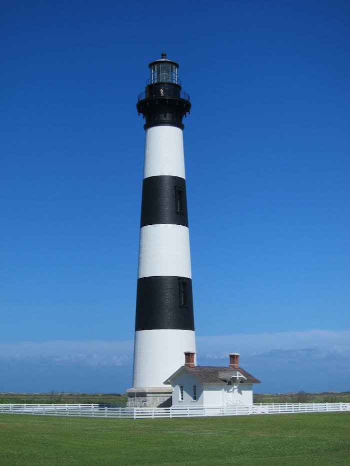 White and Black Striped Lighthouse Beside White House